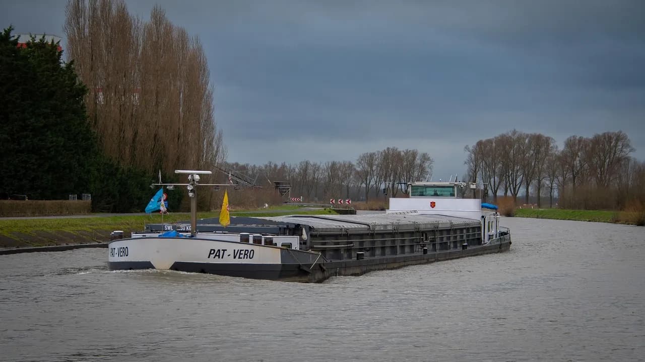 Een binnenvaartschip, een vlakbodemschip voor vrachtvervoer, vaart over een rivier of kanaal.